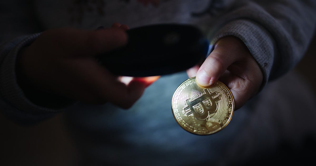 子どもの手が物理ビットコインをスマートフォンの光で照らしている
